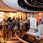 People observing a detailed architectural model of a city in an indoor exhibit space with colorful decorations.