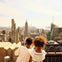 Two children look at a city skyline with tall buildings, including the Empire State Building, under a sunny sky.