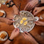 Several hands holding oysters from a plate containing oysters and lemon wedges on a wooden table.