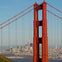 Close-up view of the Golden Gate Bridge's tower with the skyline of San Francisco visible in the background.