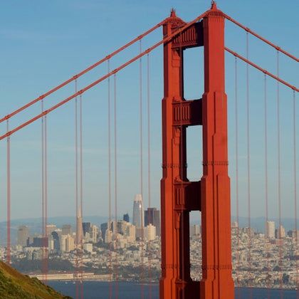 Close-up view of the Golden Gate Bridge's tower with the skyline of San Francisco visible in the background.