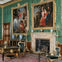 A richly decorated room with green patterned walls, ornate paintings, and antique furniture including a desk and chairs.