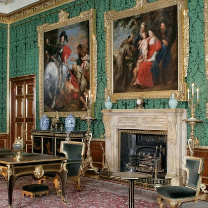 A richly decorated room with green patterned walls, ornate paintings, and antique furniture including a desk and chairs.