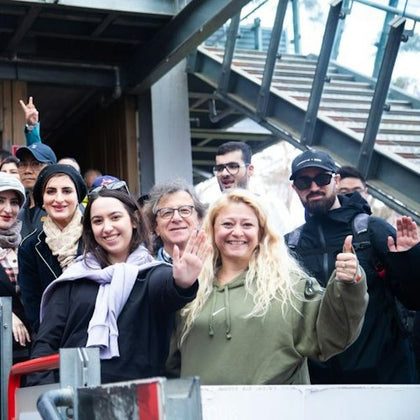 People waiting to take the red cable railway, they are all waving or smiling to the camera.