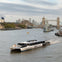 A river scene with a boat marked 'Uber Boat' cruising near Tower Bridge in London, with city buildings in the background.