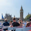 Tourists on a boat viewing Big Ben and the Houses of Parliament under a clear sky in London.