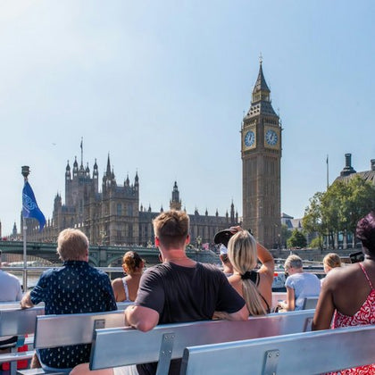 Tourists on a boat viewing Big Ben and the Houses of Parliament under a clear sky in London.