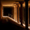 Dimly lit underground space with concrete columns, a sloped walkway, and metal railings illuminated by light.