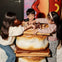 Three children playing chess on a table designed to look like a s'more, with a background featuring colorful decor.