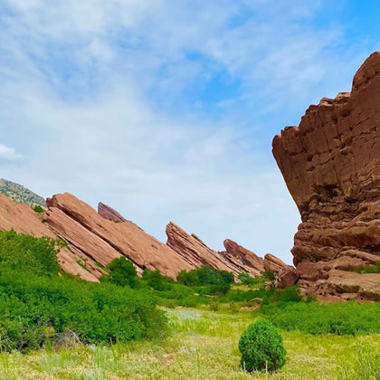A scenic view of red rock formations surrounded by green vegetation under a blue sky with scattered clouds.
