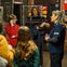 A group of people, including a guide in uniform, talking indoors near a brick wall and a door with safety signs.