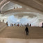 A spacious indoor architectural space with curved ceilings, a staircase, and people walking and standing on different levels.