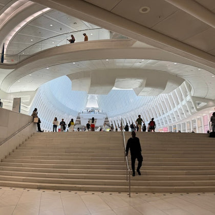 A spacious indoor architectural space with curved ceilings, a staircase, and people walking and standing on different levels.