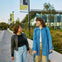 Two people walking outdoors near a modern building, smiling and engaged in conversation, under a clear sky.