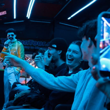 A group of people laughing and enjoying a performance by a person dressed as a singer under blue stage lighting.