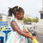 A young girl in a colorful dress looks out from the upper deck of an open-top bus on a city street.