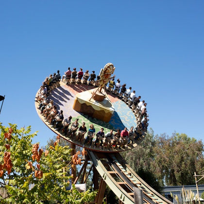 A circular amusement ride with people seated on the edge, tilting on a track against a clear blue sky.