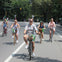 Five people riding bicycles on a tree-lined street, smiling and enjoying a sunny day.