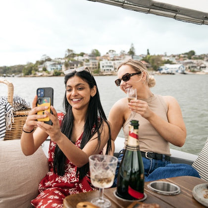 Two guests onboard a GoBoat, sharing some food \ drinks taking a selfie 