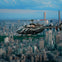 A black helicopter flies over a cityscape with many tall buildings and a park area under a mostly clear blue sky.