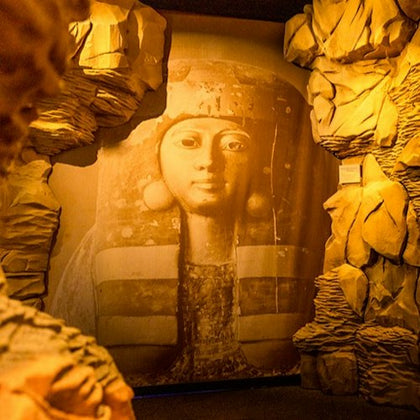 A large cultural artwork of an ancient figure's face, framed by textured walls resembling rock formations in a museum setting.