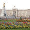 Buckingham Palace with a vibrant flower garden and the Victoria Memorial in the foreground. A flag flies above the palace.