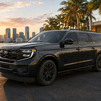 A black SUV parked in front of a palm tree-lined street with a city skyline in the background at sunset.