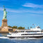 A ferry labeled 'Statue City Cruises' passing by the Statue of Liberty on a sunny day.