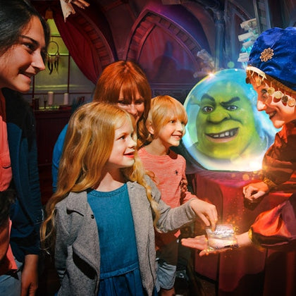 A group of children and an adult interact with a person in a costume near a glowing crystal ball displaying an animated green face.