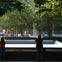 Two people stand at the edge of a large memorial fountain surrounded by trees, with more people visible in the background.