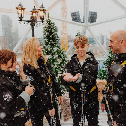 A family in winter gear stands inside a dome with fake snow and Christmas trees, smiling and enjoying the scene.