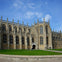 A historic stone building with large Gothic-style windows and spires, surrounded by a green lawn under a blue sky.