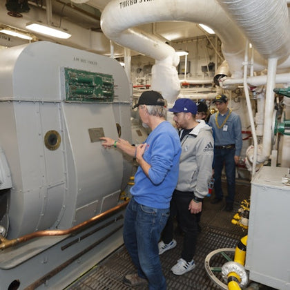 A group of people examining machinery in an industrial setting with pipes and equipment visible.