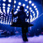 A silhouetted person sits on a swing against a background of glowing circular lights and fog in a dark setting.