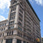 A multistory historic-style building with detailed architecture, fire escapes, and a traffic light in the foreground.