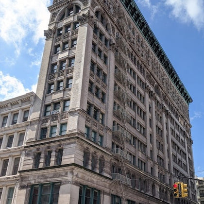 A multistory historic-style building with detailed architecture, fire escapes, and a traffic light in the foreground.