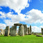Stonehenge under a partly cloudy blue sky, surrounded by green grass.