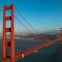 The Golden Gate Bridge spanning over water, with a view of the city and hills in the background under a clear sky.
