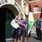 Two people stand smiling in front of a museum entrance, with a staff member and a flag nearby on a sunny day.