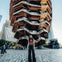 Woman standing in front of the Vessel, a honeycomb-like structure, with surrounding people and buildings in the background.
