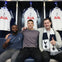 Three men sit on a bench in a locker room, each giving a thumbs-up, with Tottenham Hotspur football jerseys hanging behind them.