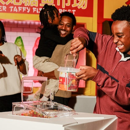 A group of people enjoying a candy store. A person is filling a container with candy, while others smile in the background.