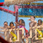 Children and a man standing on a water play structure, enjoying water sprays under a blue sky on a sunny day.