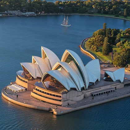 Aerial view of the Sydney Opera House with its iconic white shell-like roof, surrounded by water and adjacent greenery.