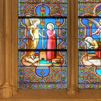 A stained glass window depicting a biblical scene with an angel and a praying figure in a colorful, intricate design.