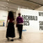 Two people walking in a modern art gallery with visible signage for the Archibald 2025 and Wynne prizes.