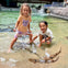 Two children interacting with rays in a shallow pool at an indoor aquarium exhibit, smiling and enjoying the activity.