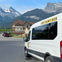 A white van labeled "The Fairy Bus" parked in a residential area with mountains in the background.