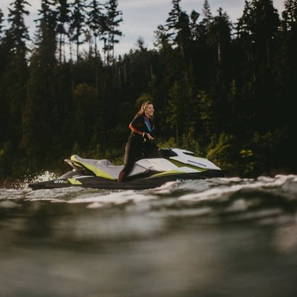 Person riding a jet ski on the water with a forested area in the background.