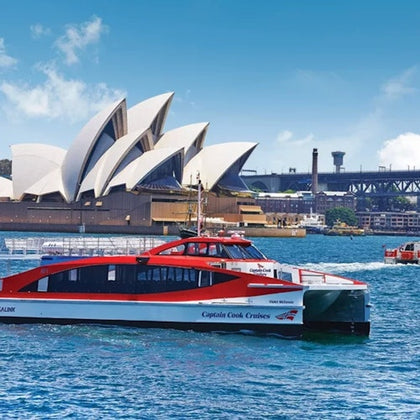 A modern red and white ferry on the water with the Sydney Opera House and Sydney Harbour Bridge in the background.